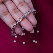 A sterling silver wire knot trendy bracelet held in a person's hand, with rose gold accents and silver beads scattered on a red background.